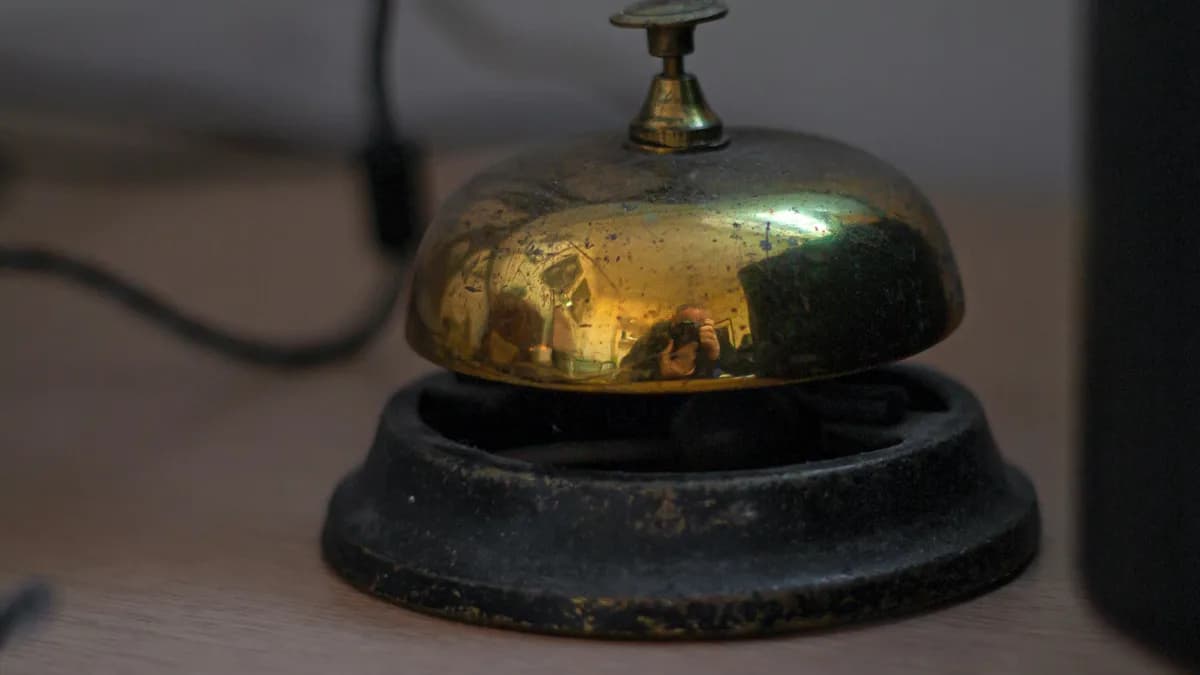 Sino de balcão de latão antigo sobre mesa de madeira, sem ninguém para atender, representando o chatbot de WhatsApp que responde na hora mas não resolve o orçamento