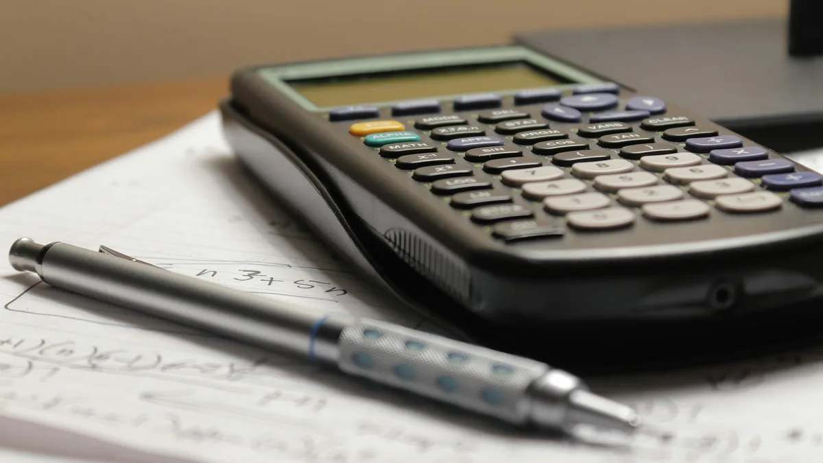 Calculadora científica sobre folhas com contas feitas à mão e uma lapiseira, em uma mesa de madeira, representando o cálculo do custo real de contratar uma secretária